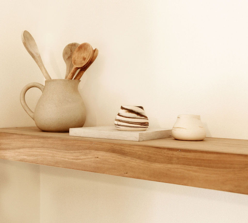 A rustic wooden shelf with ceramic cups and kitchen utensils, showcasing a minimalistic and warm home decor style.