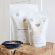 Mexican ceremonial cacao packages with a blue bowl of cacao powder, showcasing premium quality, organic, award-winning product.