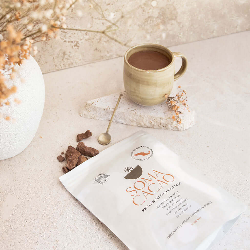Organic Mexican ceremonial cacao package beside a cup of cacao drink and decorative elements on a light surface.