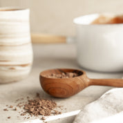 Hand-crafted wooden measuring spoon with ceremonial cacao, set against a serene kitchen background. Premium quality design.