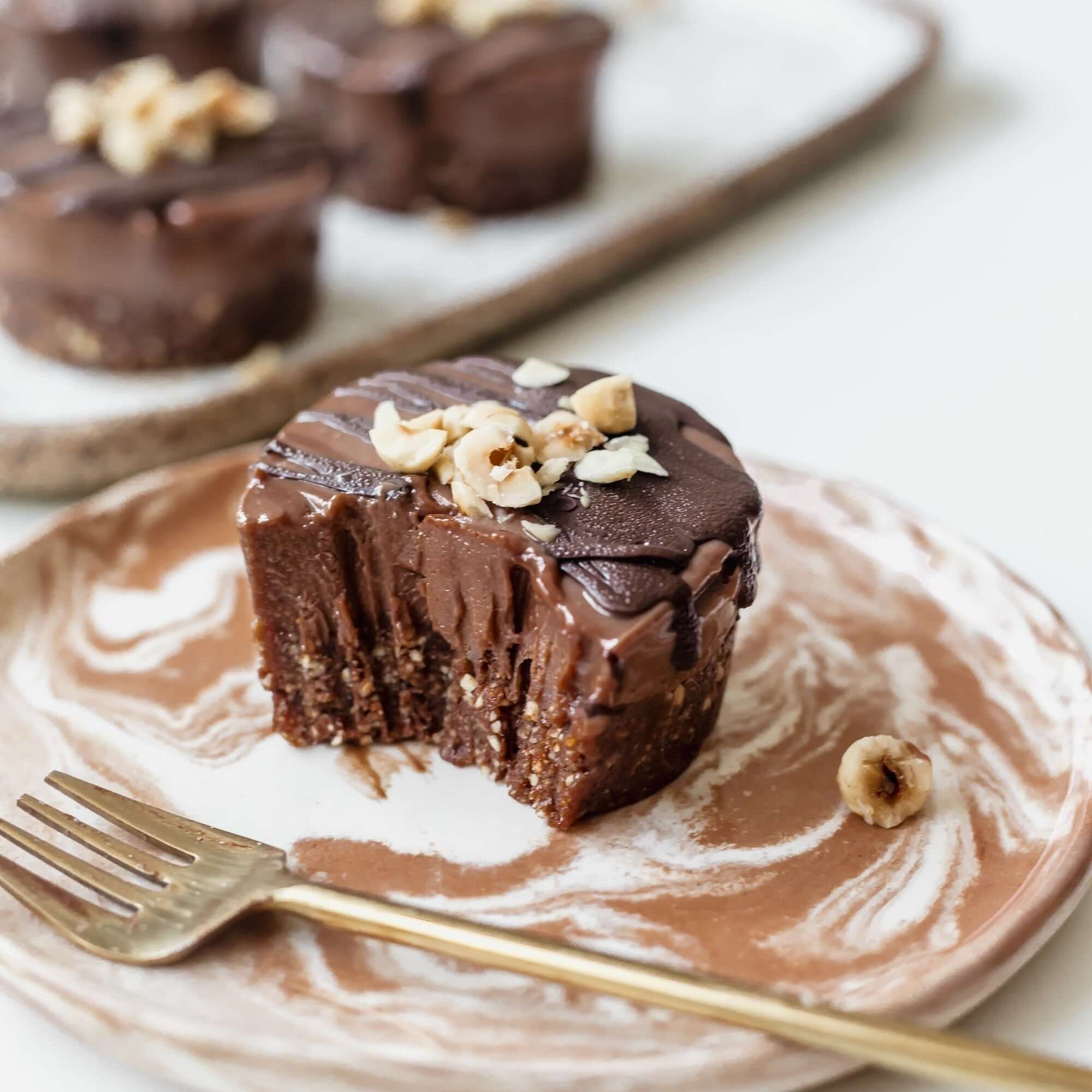 Vegan mini chocolate hazelnut cheesecake on a plate, topped with crushed hazelnuts and chocolate glaze.
