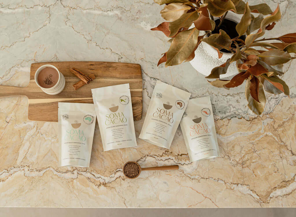 assortment of SOMA CACAO ceremonial cacao packs on a marble surface with a cup and spoon, showcasing premium quality flavors.