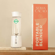 Soma Portable Blender beside its packaging on a wooden shelf, ideal for making premium ceremonial cacao anywhere.