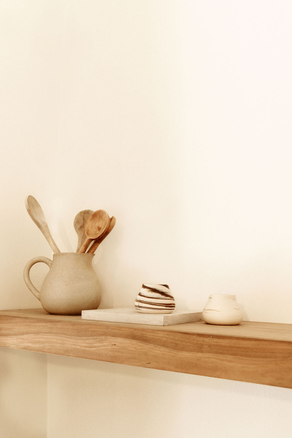A rustic wooden shelf with ceramic cups and kitchen utensils, showcasing a minimalistic and warm home decor style.
