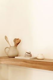 A rustic wooden shelf with ceramic cups and kitchen utensils, showcasing a minimalistic and warm home decor style.