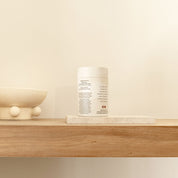 White container with product information on a wooden shelf next to a decorative bowl and stone slab.