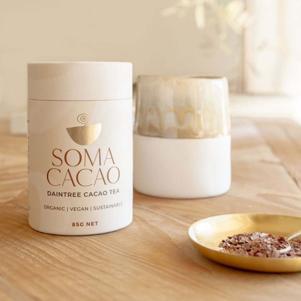Daintree Cacao Tea packaging with a cup and saucer on a wooden table, showcasing premium organic cacao.