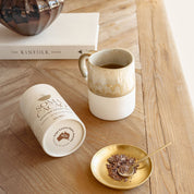 Daintree Cacao Tea in a stylish setting with a mug, golden spoon, and cacao husks on a wooden table.