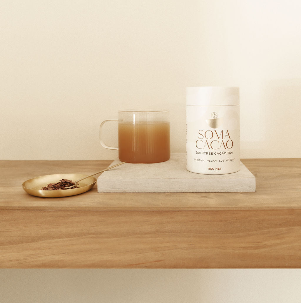 Daintree Cacao Tea in elegant packaging with brewed tea in a glass, served on a wooden surface with a golden spoon.