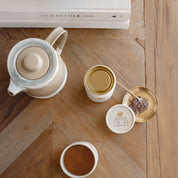 Daintree cacao tea served in a cup with a teapot and premium cacao jar on a wooden table.