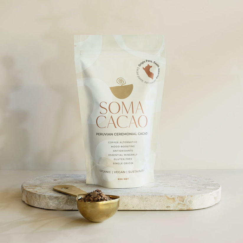 Peruvian Ceremonial Cacao package on a marble surface with a gold scoop and cacao nibs.