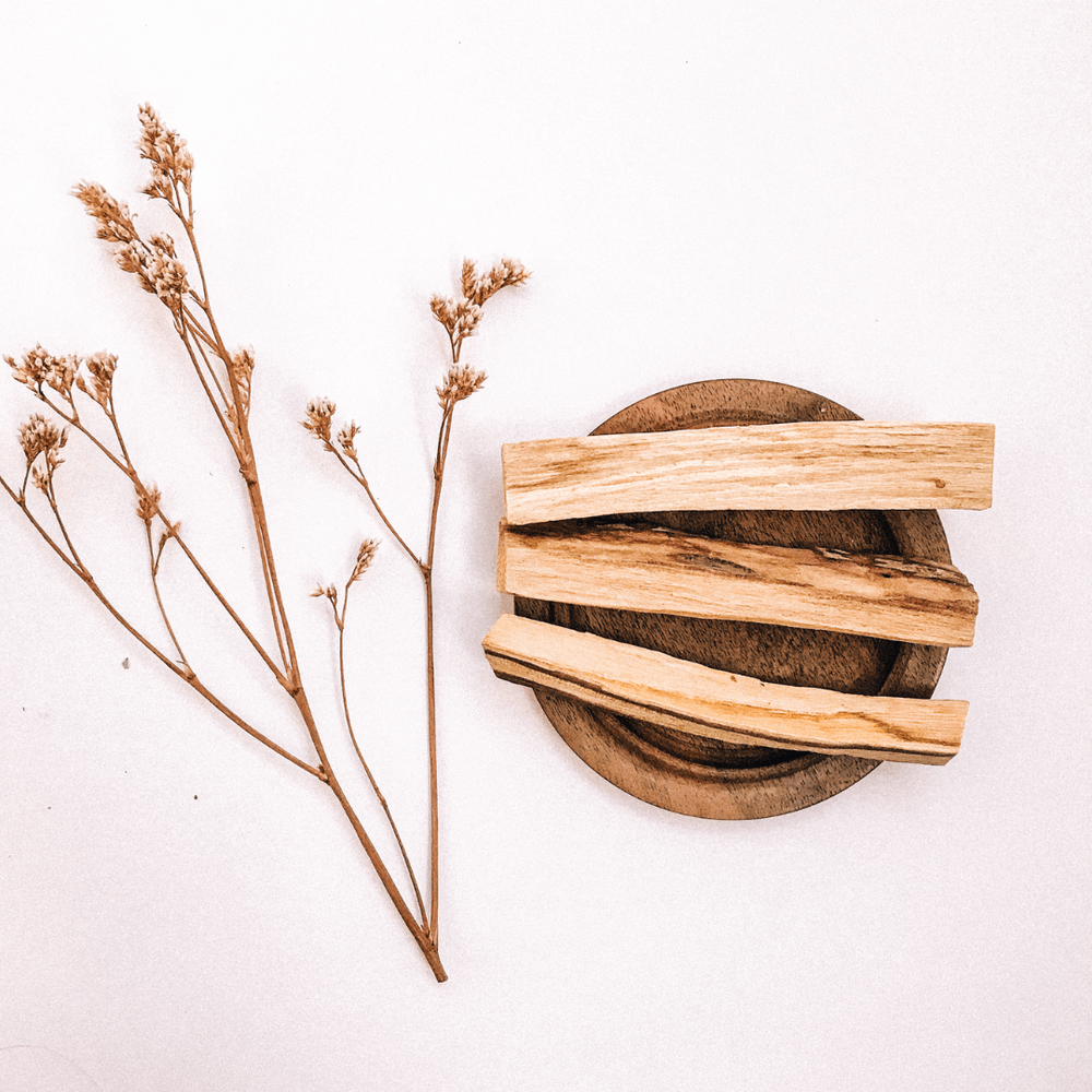 Wild-harvested sustainable Palo Santo sticks on a wooden plate with dried flowers, symbolizing premium quality and ceremony.
