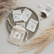 Reusable organic cotton tea bags arranged on a ceramic plate with tea leaves, showcasing premium quality and eco-friendliness.